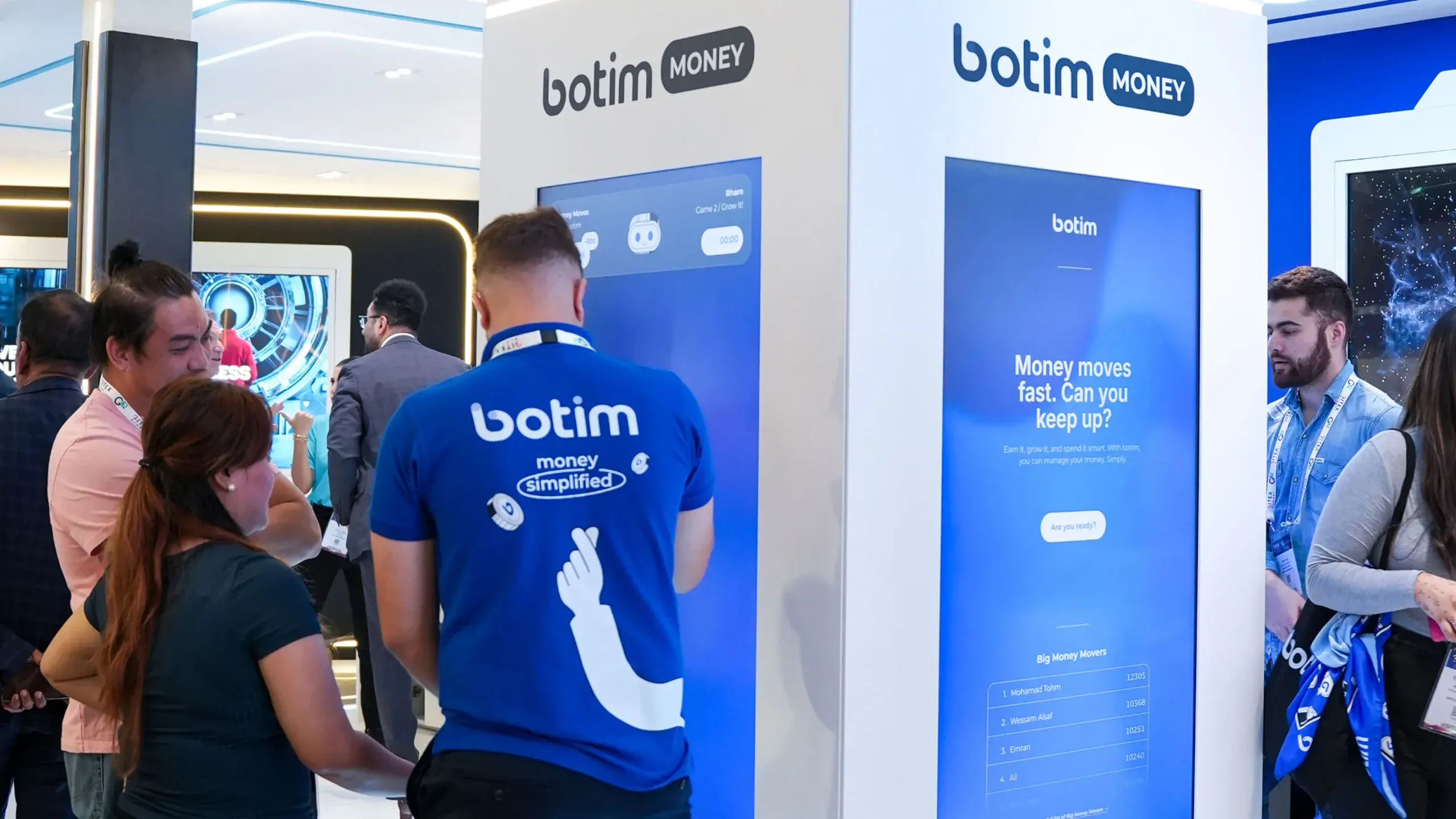 Visitors playing Money Moves on tall touchscreens at the botim booth.