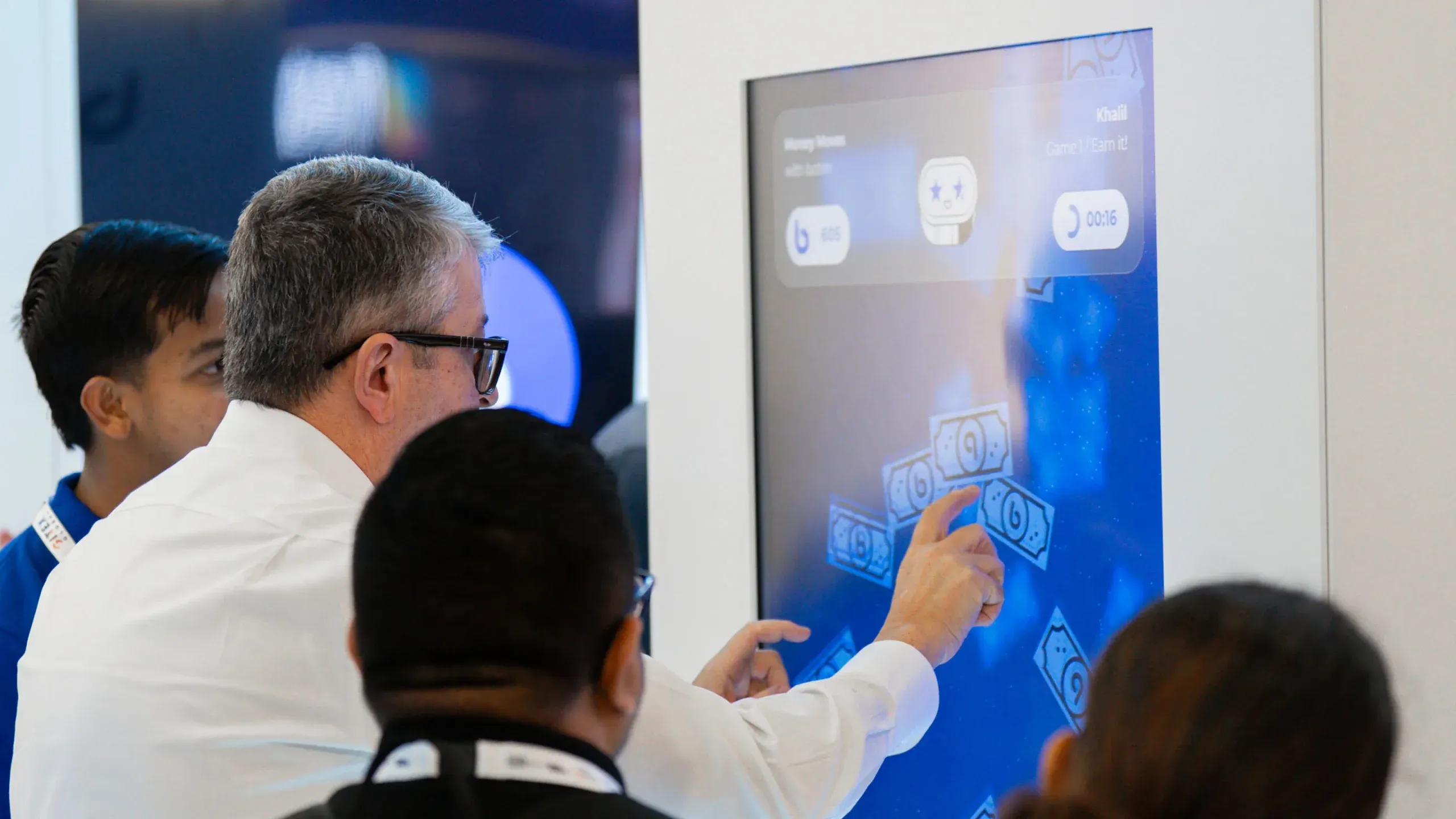 Two visitors lean in to play Money Moves on a large vertical screen.