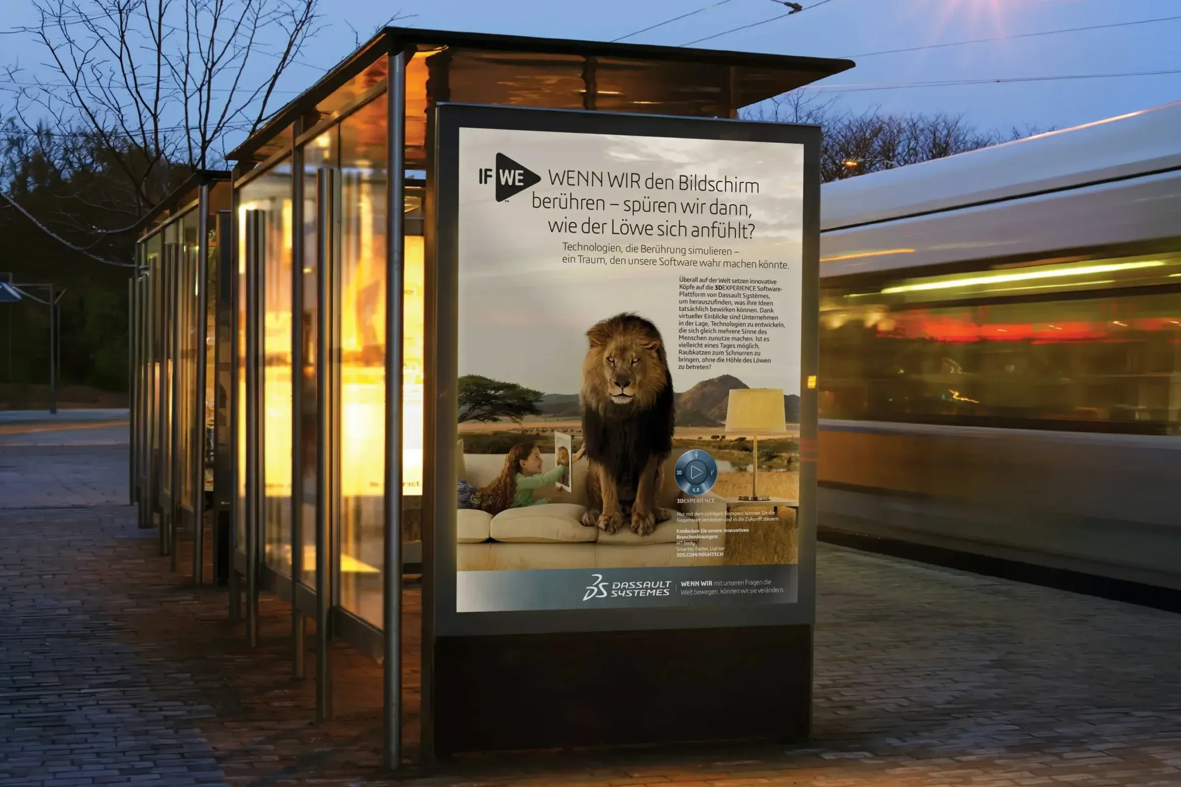 A Dassault Systèmes IF WE poster in a lit bus shelter at dusk, showing a girl on a sofa touching a tablet beside a lion