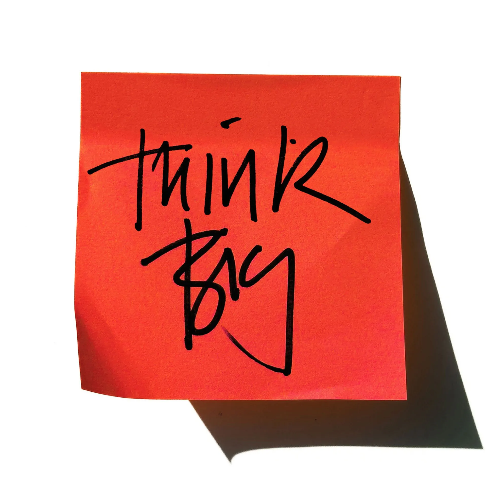 A bright orange sticky note on a white background with the handwritten text "think Big" in black marker.