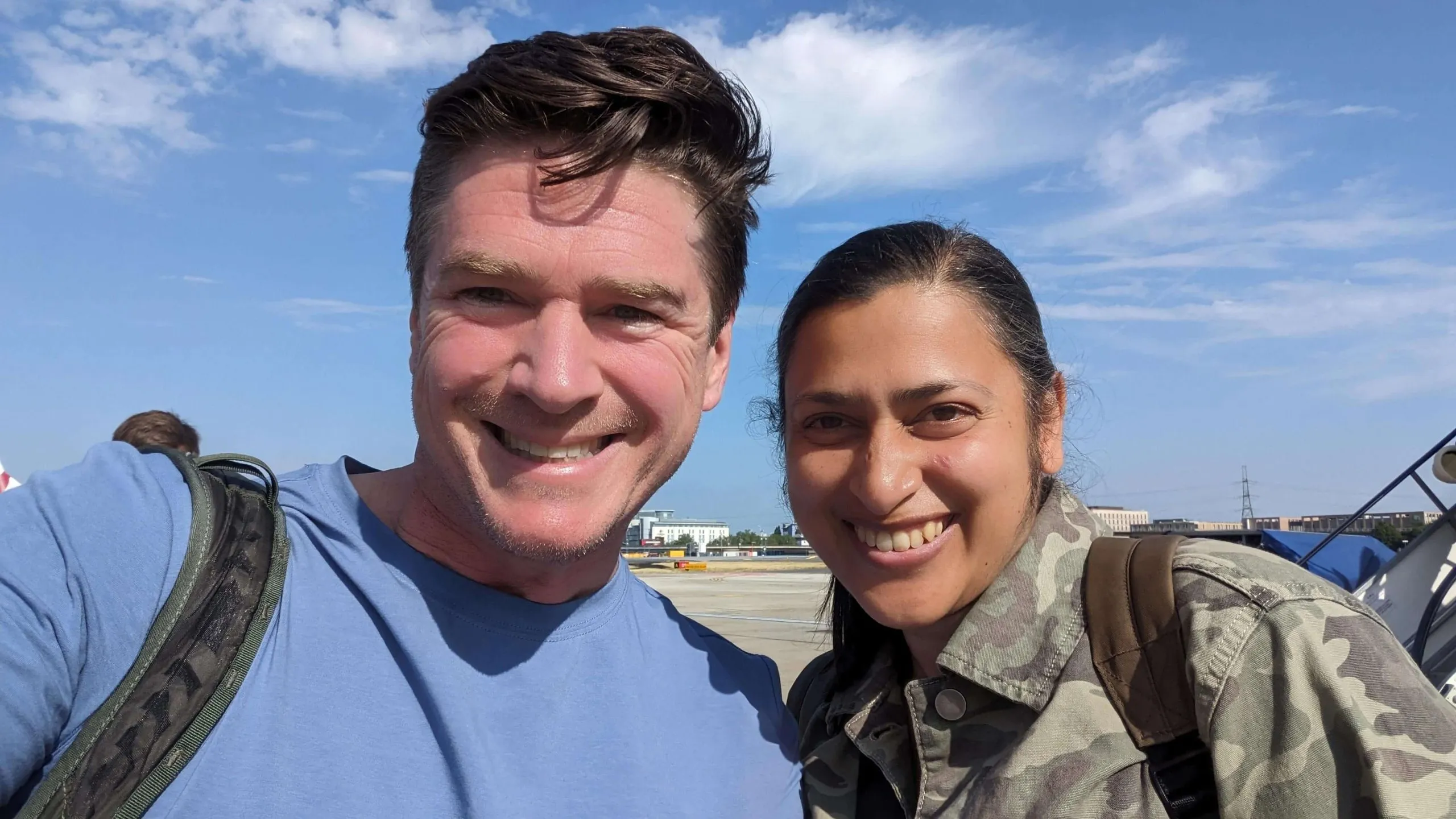 Two colleagues, Don and Mayuri, smile for a selfie on an airfield in Tanzania.