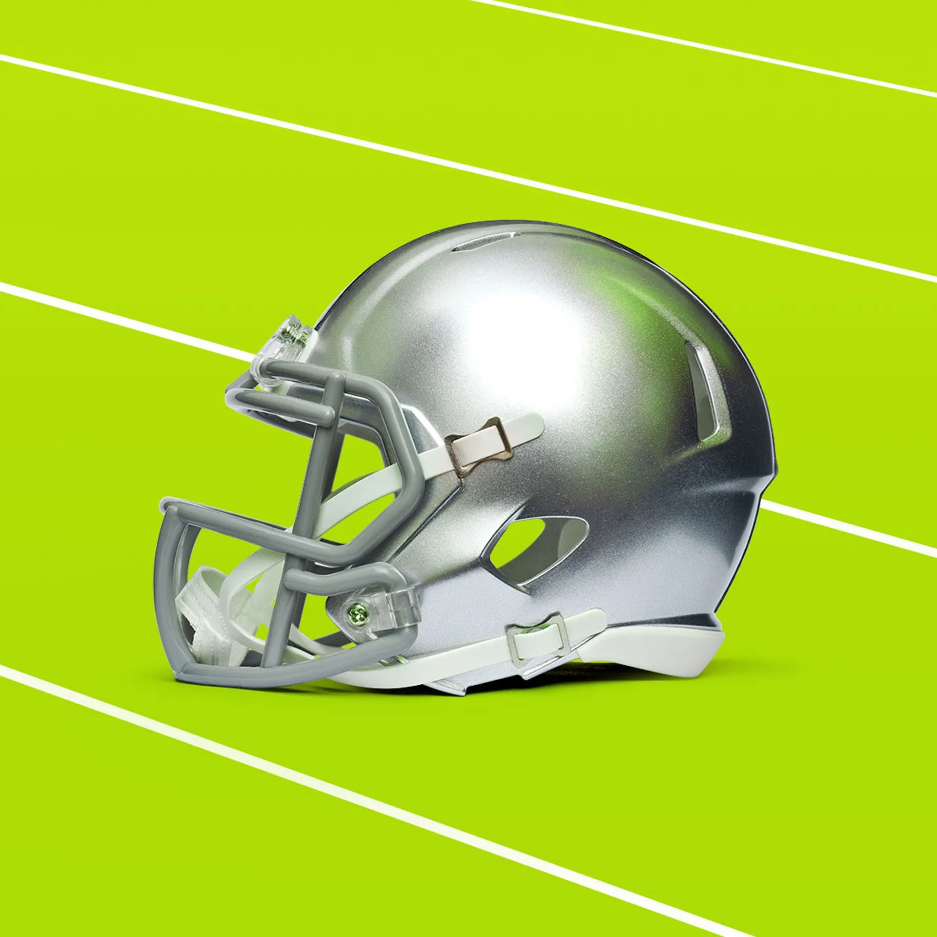 A metallic silver football helmet with a gray facemask rests on a bright lime green surface with diagonal white yard lines.