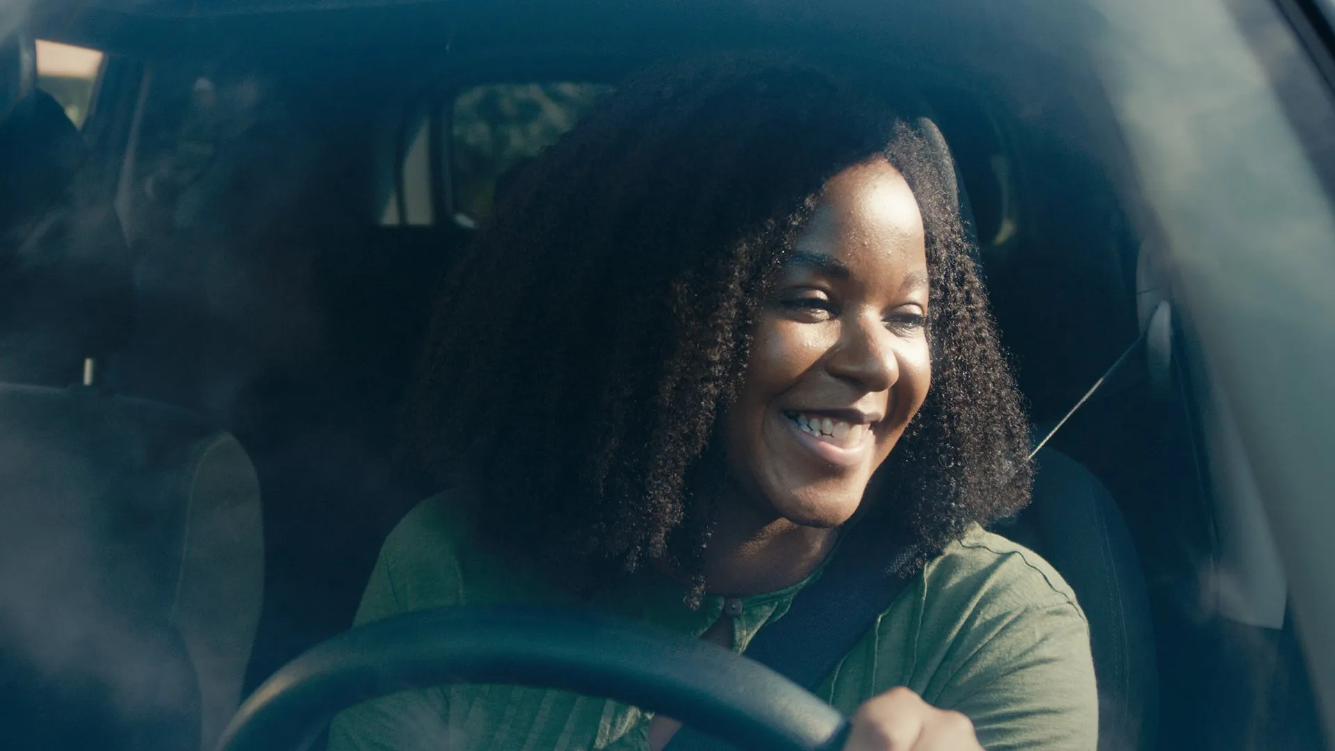 A woman smiling at the wheel of a car