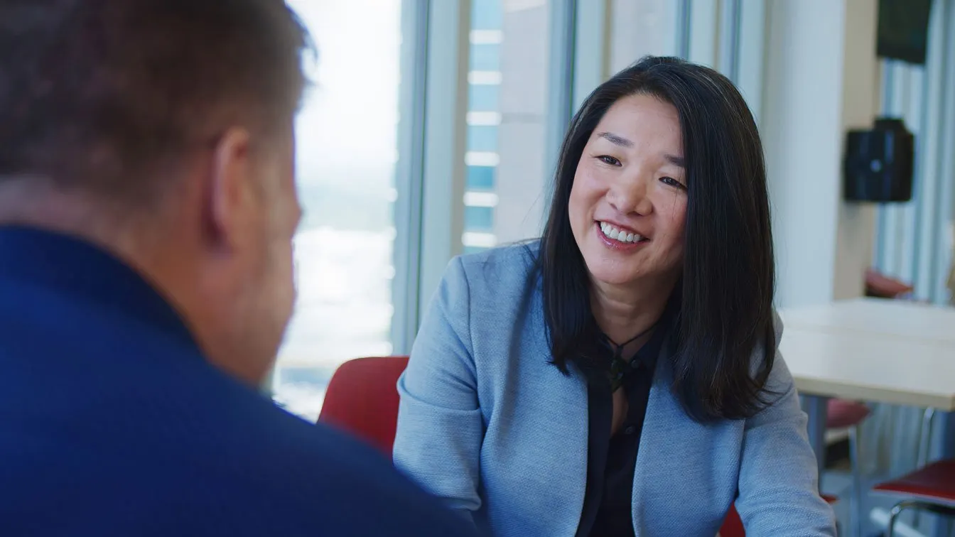 Smiling woman in a light blue blazer talking with a man in a blue shirt in an office.